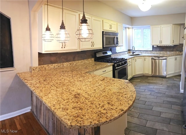 kitchen featuring light stone counters, a peninsula, dark wood-style flooring, a sink, and appliances with stainless steel finishes