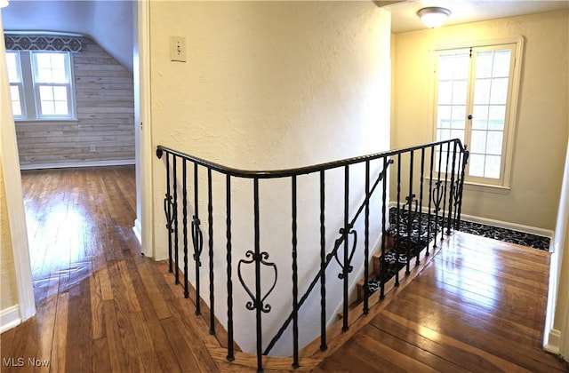 corridor with a textured wall, wood walls, an upstairs landing, baseboards, and hardwood / wood-style floors