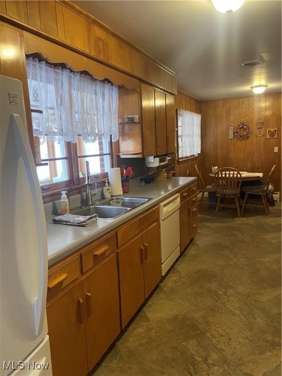 kitchen with wooden walls, refrigerator, white dishwasher, a healthy amount of sunlight, and a sink