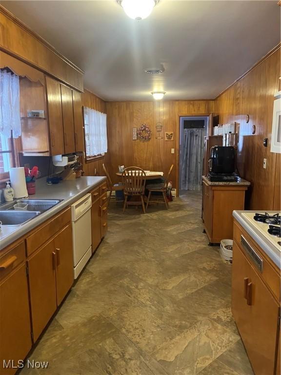 kitchen with wood walls, a sink, light countertops, brown cabinets, and dishwasher