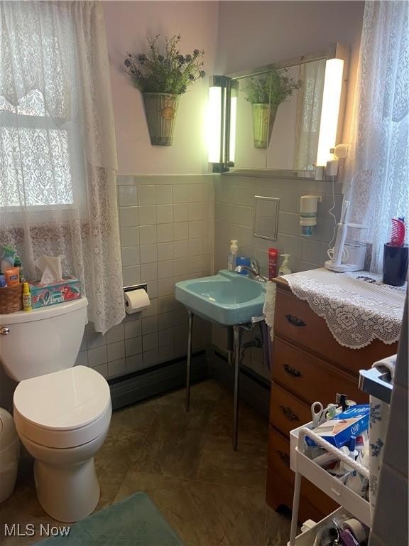 half bathroom with toilet, a sink, tile walls, wainscoting, and tile patterned floors