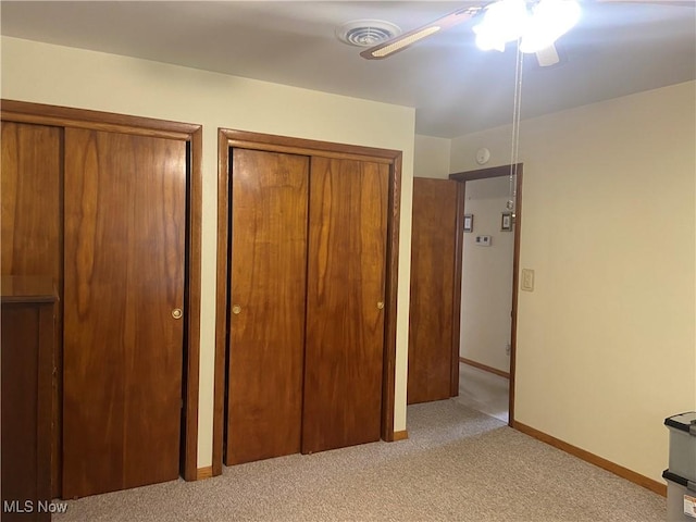 unfurnished bedroom with two closets, visible vents, a ceiling fan, light carpet, and baseboards