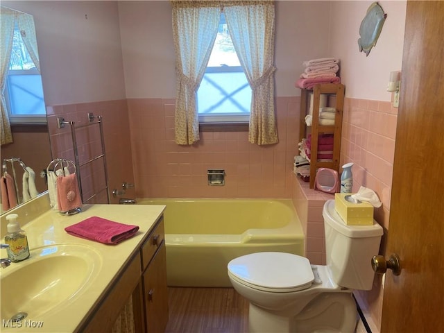 bathroom with tile walls, toilet, wainscoting, vanity, and a bath