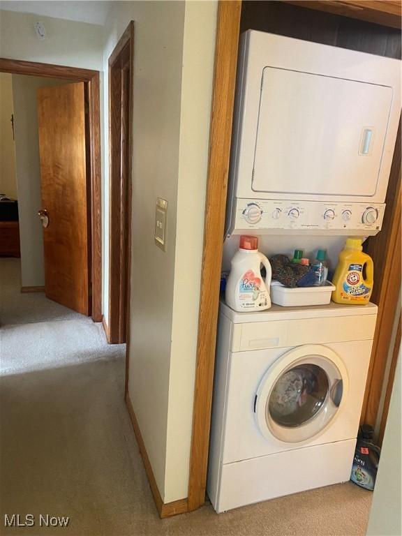 clothes washing area featuring laundry area, stacked washer / dryer, carpet flooring, and baseboards