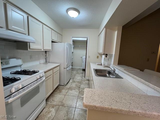 kitchen featuring tasteful backsplash, a sink, a textured ceiling, white appliances, and under cabinet range hood