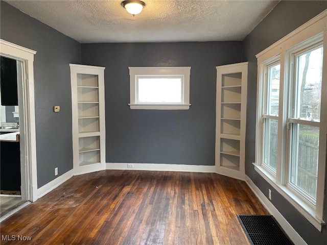 spare room featuring baseboards, a textured ceiling, visible vents, and dark wood-type flooring