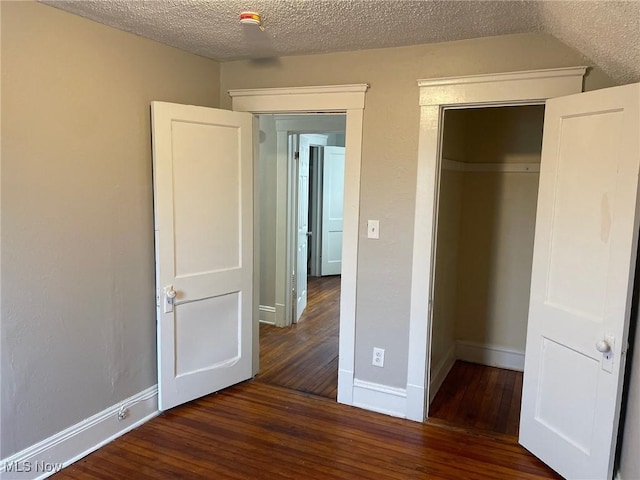 unfurnished bedroom with a textured ceiling, a closet, hardwood / wood-style flooring, and baseboards