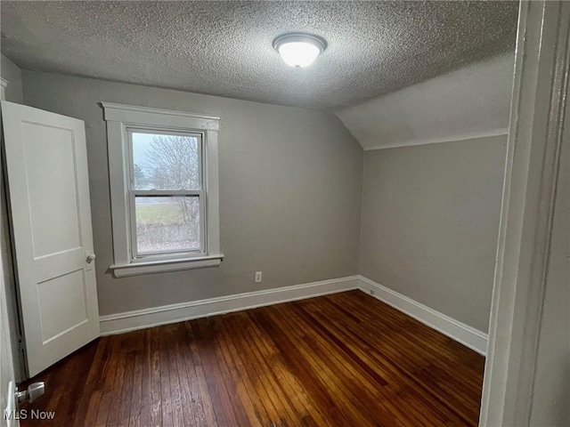 additional living space with lofted ceiling, a textured ceiling, hardwood / wood-style flooring, and baseboards