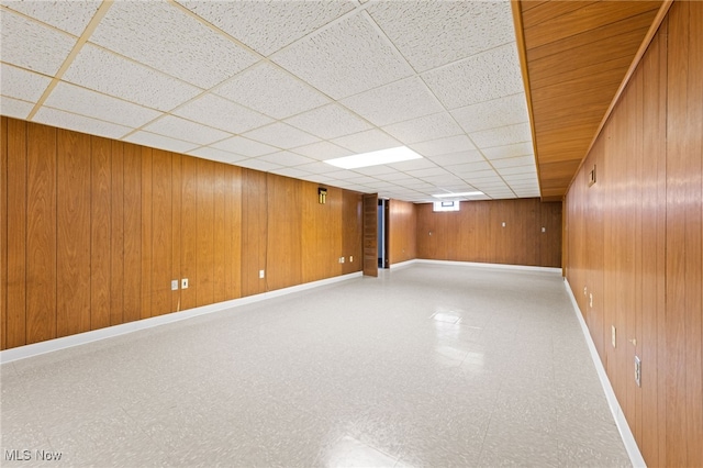 finished below grade area with baseboards, wooden walls, a paneled ceiling, and tile patterned floors