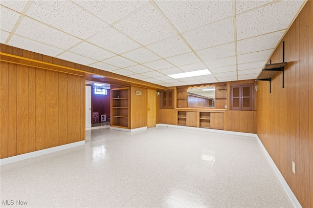 finished below grade area with a paneled ceiling, wood walls, baseboards, and tile patterned floors