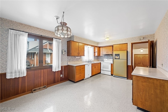 kitchen featuring white appliances, wallpapered walls, brown cabinetry, light countertops, and a sink