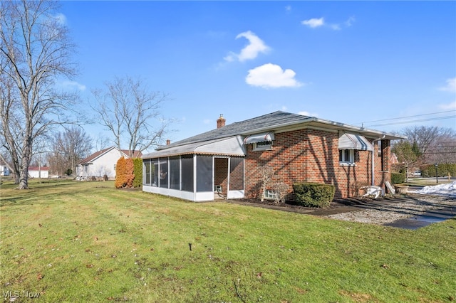 rear view of property featuring a sunroom, brick siding, a lawn, and a chimney