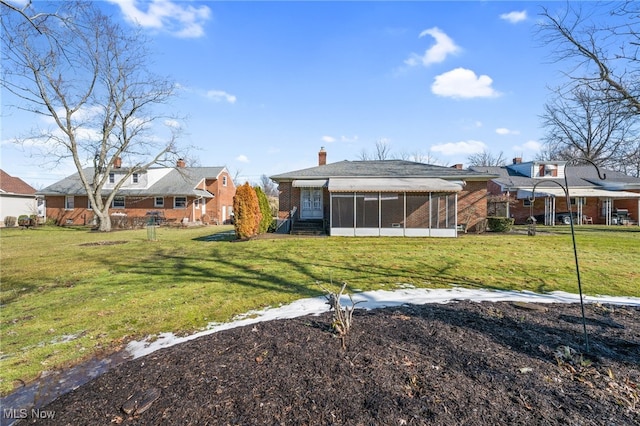 rear view of property featuring brick siding, a lawn, and a sunroom