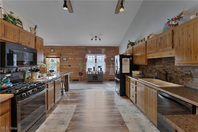 kitchen featuring tasteful backsplash, light wood-style flooring, a sink, wood walls, and black appliances