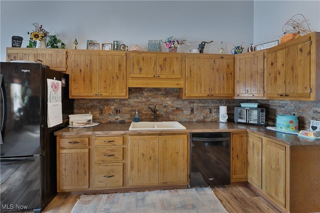 kitchen with black appliances, tasteful backsplash, light wood finished floors, and a sink