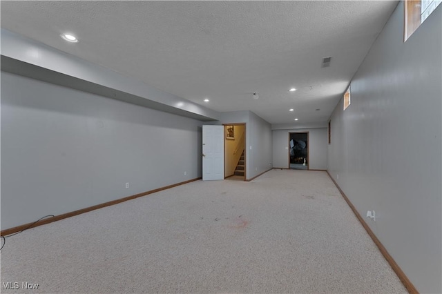 finished basement featuring a textured ceiling, recessed lighting, light colored carpet, baseboards, and stairs