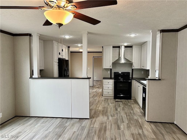 kitchen featuring dark countertops, wall chimney exhaust hood, light wood-style flooring, black appliances, and white cabinetry