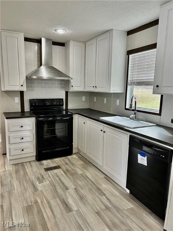 kitchen featuring dark countertops, a sink, wall chimney range hood, and black appliances