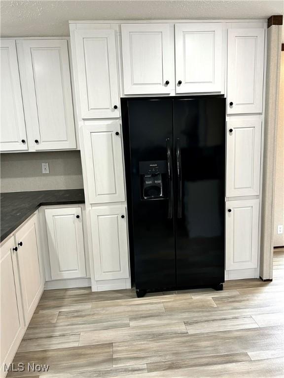 kitchen featuring light wood finished floors, dark countertops, white cabinetry, a textured ceiling, and black fridge