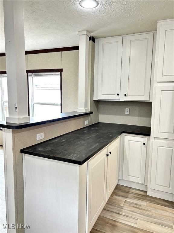 kitchen featuring dark countertops, light wood-style flooring, white cabinetry, a textured ceiling, and a peninsula