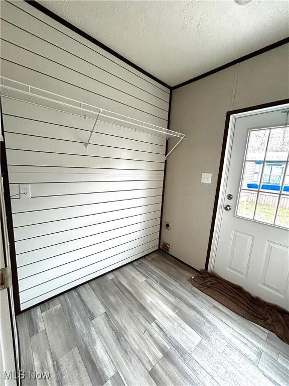 interior space featuring laundry area, wood walls, a textured ceiling, and wood finished floors