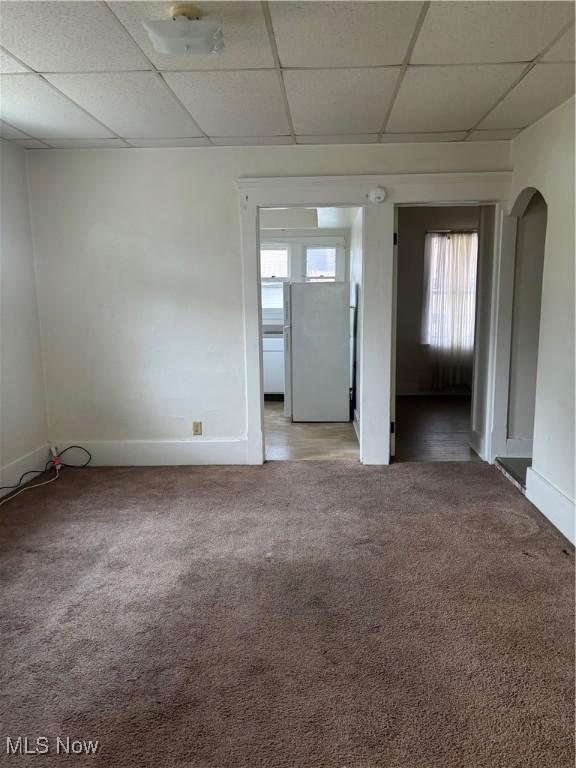 empty room featuring light carpet, a drop ceiling, arched walkways, and baseboards