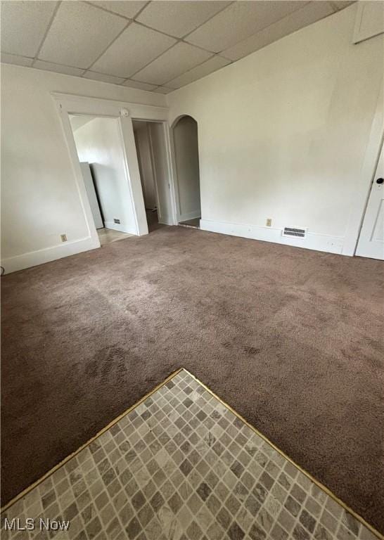 carpeted spare room featuring baseboards, visible vents, arched walkways, and a drop ceiling