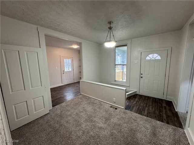 entrance foyer featuring baseboards, visible vents, dark wood finished floors, a textured ceiling, and dark carpet