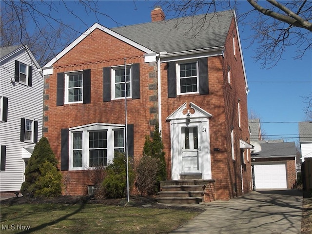 view of front of home with brick siding, roof with shingles, a chimney, an outdoor structure, and driveway