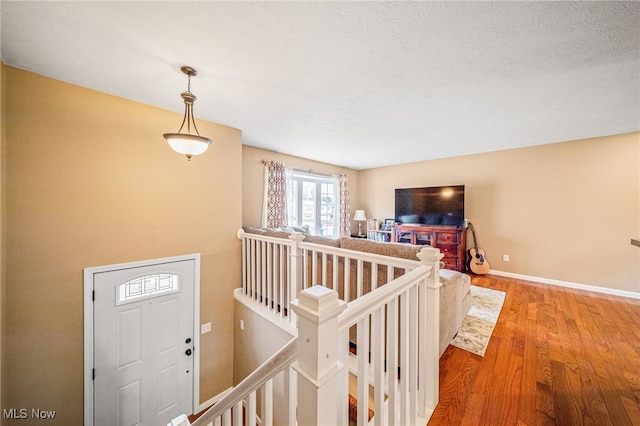 hall featuring baseboards, light wood finished floors, an upstairs landing, and a textured ceiling