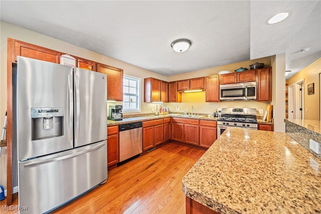 kitchen with light stone counters, brown cabinets, stainless steel appliances, light wood-style flooring, and a sink