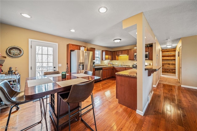 kitchen with appliances with stainless steel finishes, light wood-type flooring, brown cabinets, and a peninsula