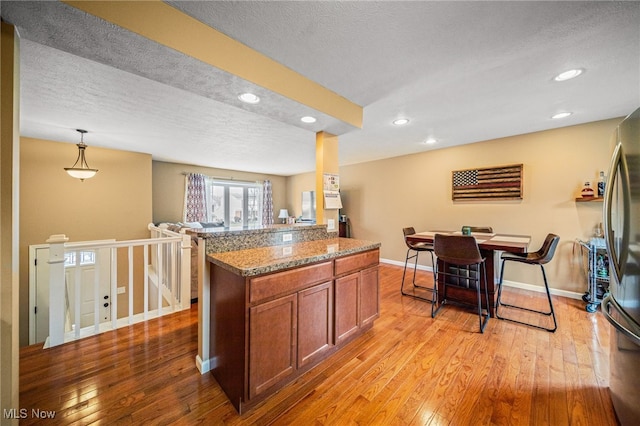 kitchen featuring brown cabinets, recessed lighting, light wood-style flooring, freestanding refrigerator, and a textured ceiling