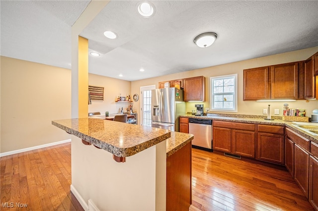 kitchen featuring brown cabinetry, appliances with stainless steel finishes, a kitchen breakfast bar, a textured ceiling, and light wood-style floors