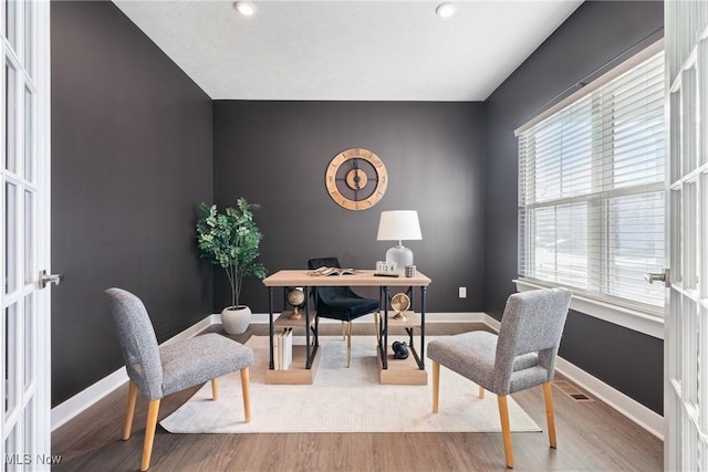 office space featuring visible vents, an accent wall, baseboards, and wood finished floors