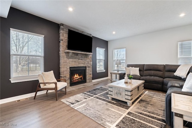 living area featuring a healthy amount of sunlight, a fireplace, visible vents, and wood finished floors