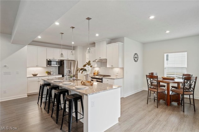 kitchen featuring appliances with stainless steel finishes, light wood-type flooring, an island with sink, and a breakfast bar area