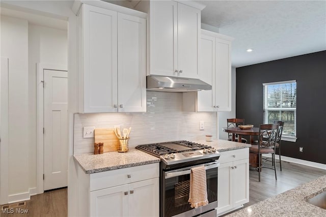 kitchen featuring under cabinet range hood, white cabinets, baseboards, light stone countertops, and stainless steel range with gas stovetop