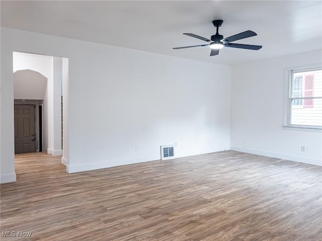 spare room with baseboards, visible vents, arched walkways, ceiling fan, and wood finished floors