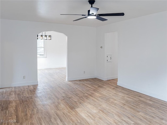 empty room featuring light wood-style flooring, arched walkways, ceiling fan, and baseboards