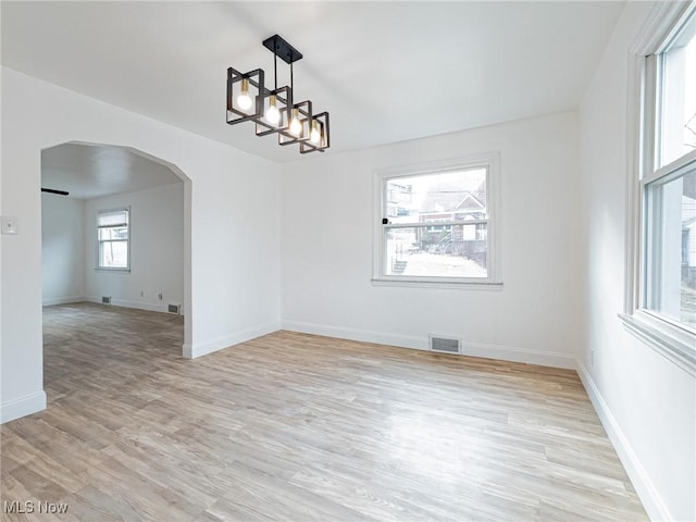 empty room with light wood finished floors, visible vents, arched walkways, baseboards, and an inviting chandelier