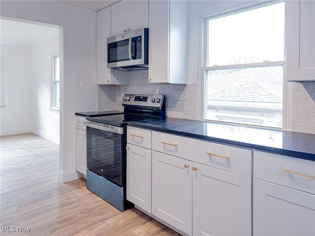 kitchen with stainless steel appliances, backsplash, dark stone counters, white cabinetry, and light wood-type flooring