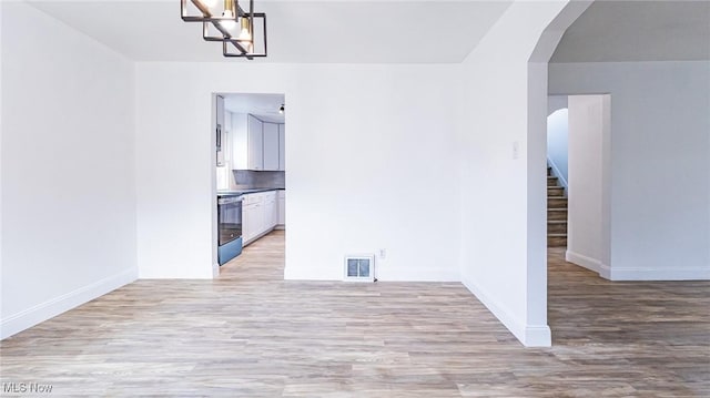 interior space featuring arched walkways, visible vents, light wood-style flooring, baseboards, and stairs