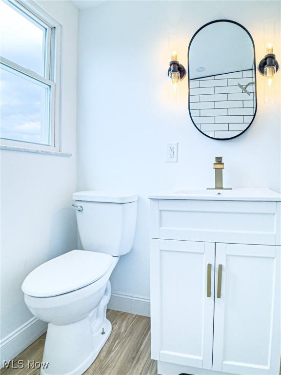 half bathroom featuring toilet, baseboards, wood finished floors, and vanity