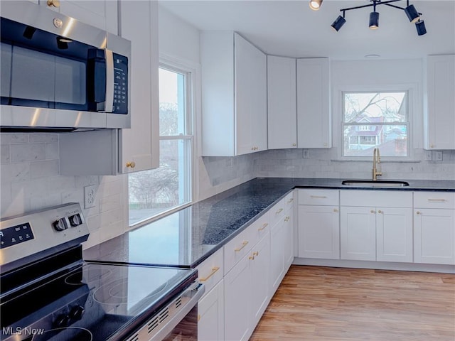 kitchen featuring stainless steel appliances, a sink, white cabinets, backsplash, and light wood finished floors