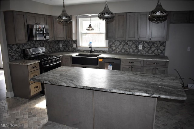 kitchen featuring light stone counters, a sink, appliances with stainless steel finishes, backsplash, and a center island