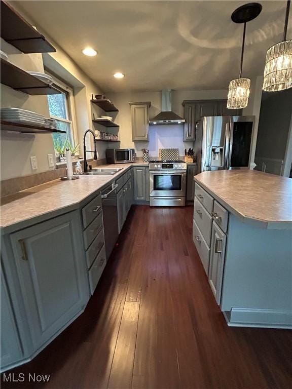 kitchen with appliances with stainless steel finishes, gray cabinets, wall chimney range hood, open shelves, and a sink