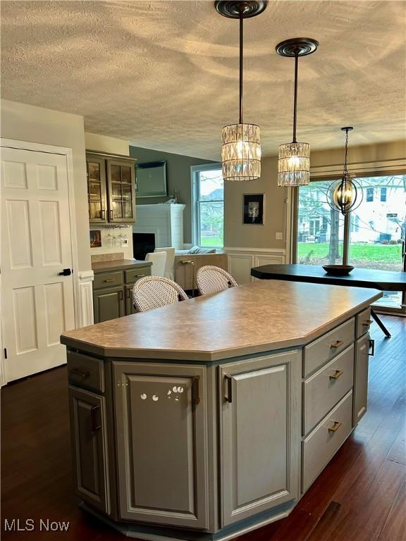 kitchen with a textured ceiling, a kitchen island, light countertops, hanging light fixtures, and dark wood finished floors