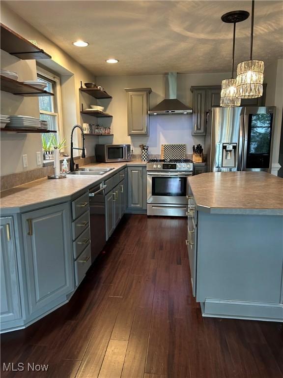 kitchen with open shelves, gray cabinets, appliances with stainless steel finishes, a sink, and wall chimney range hood