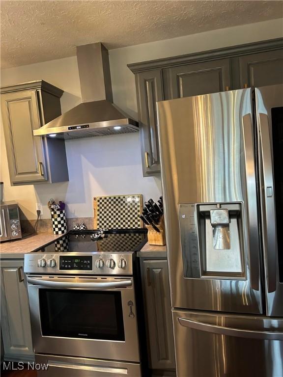 kitchen featuring wall chimney exhaust hood, a textured ceiling, stainless steel appliances, and light countertops